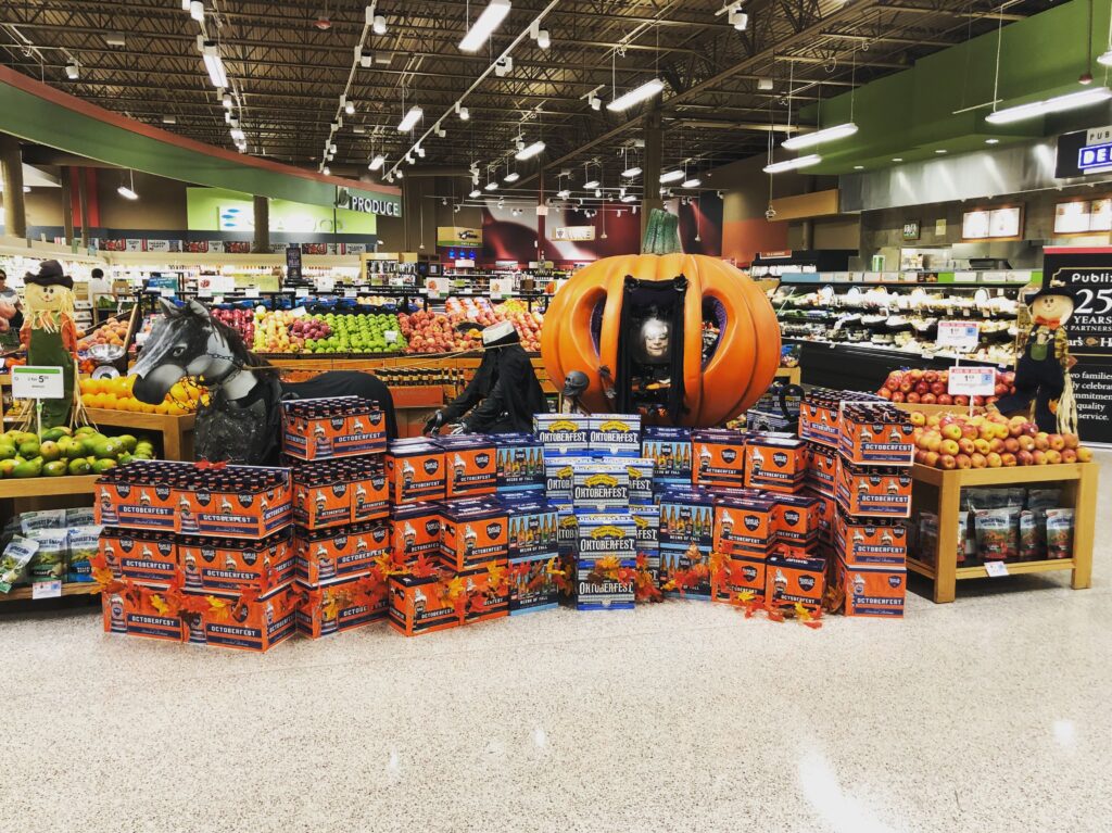 A grocery store's early fall display with Oktoberfest beer and Halloween decorations highlights seasonal marketing trends to boost sales and engagement.